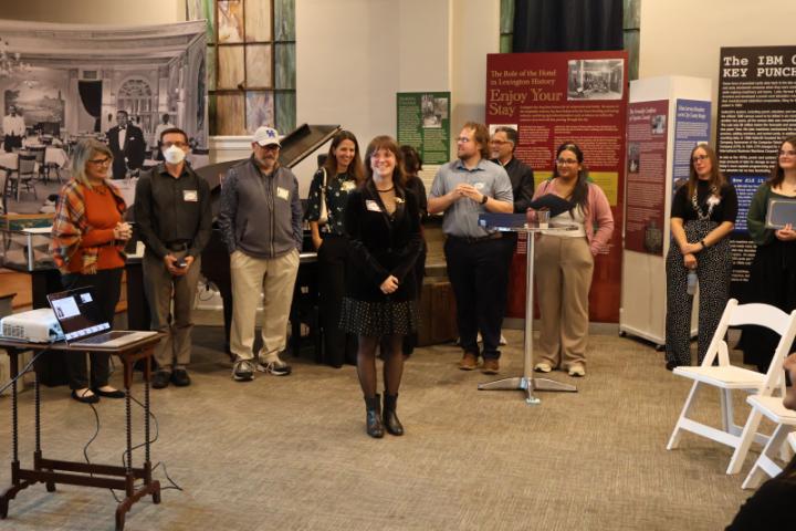 A picture of graduate student, Kimberly Cook, with multiple faculty members, students, and the THM speaker in the background.