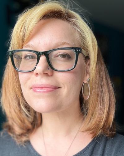 A woman with shoulder-length blonde hair and black-framed glasses smiling at the camera.
