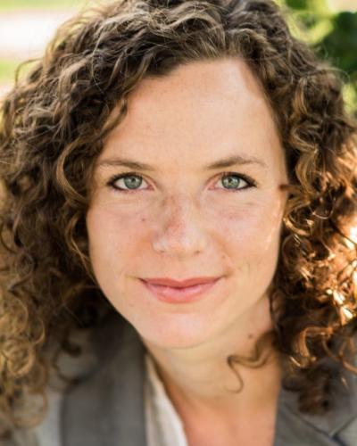 A woman with curly brown hair and green eyes smiling at the camera.