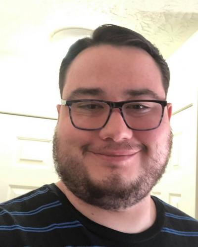 A man wearing glasses and a striped shirt smiles at the camera.