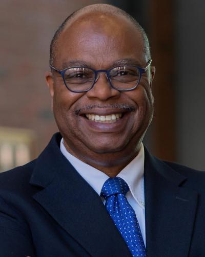 A man in a suit and blue tie smiles while looking at the camera.