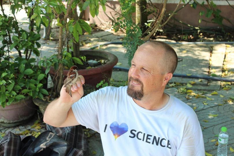 A photo of Dr. Martin holding a bird outside with some greenery in the background.