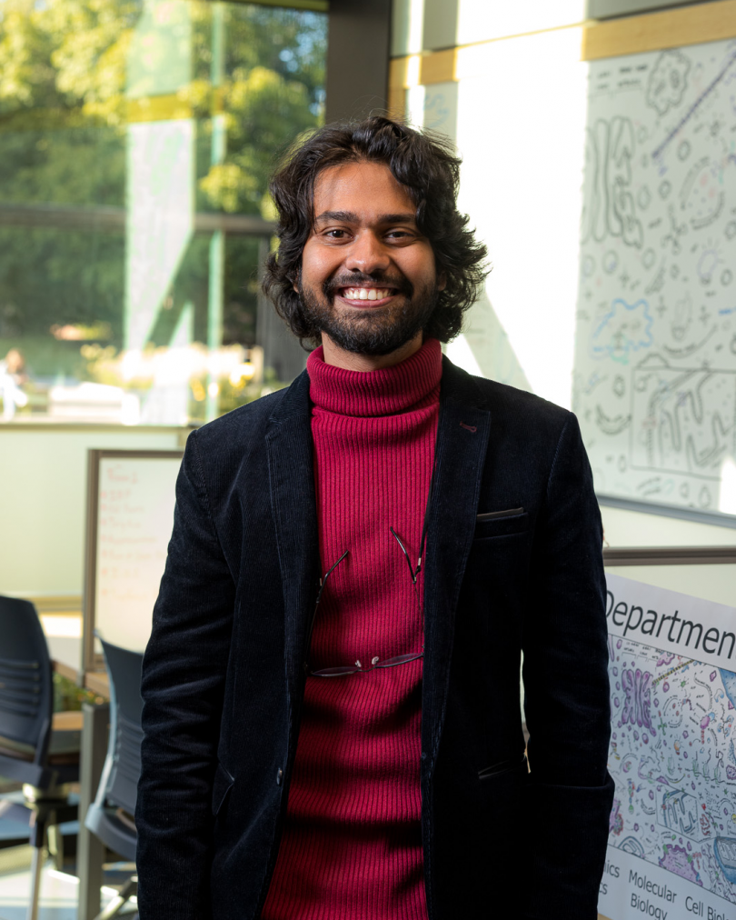 D'Souza smiling in a red sweater and black blazer